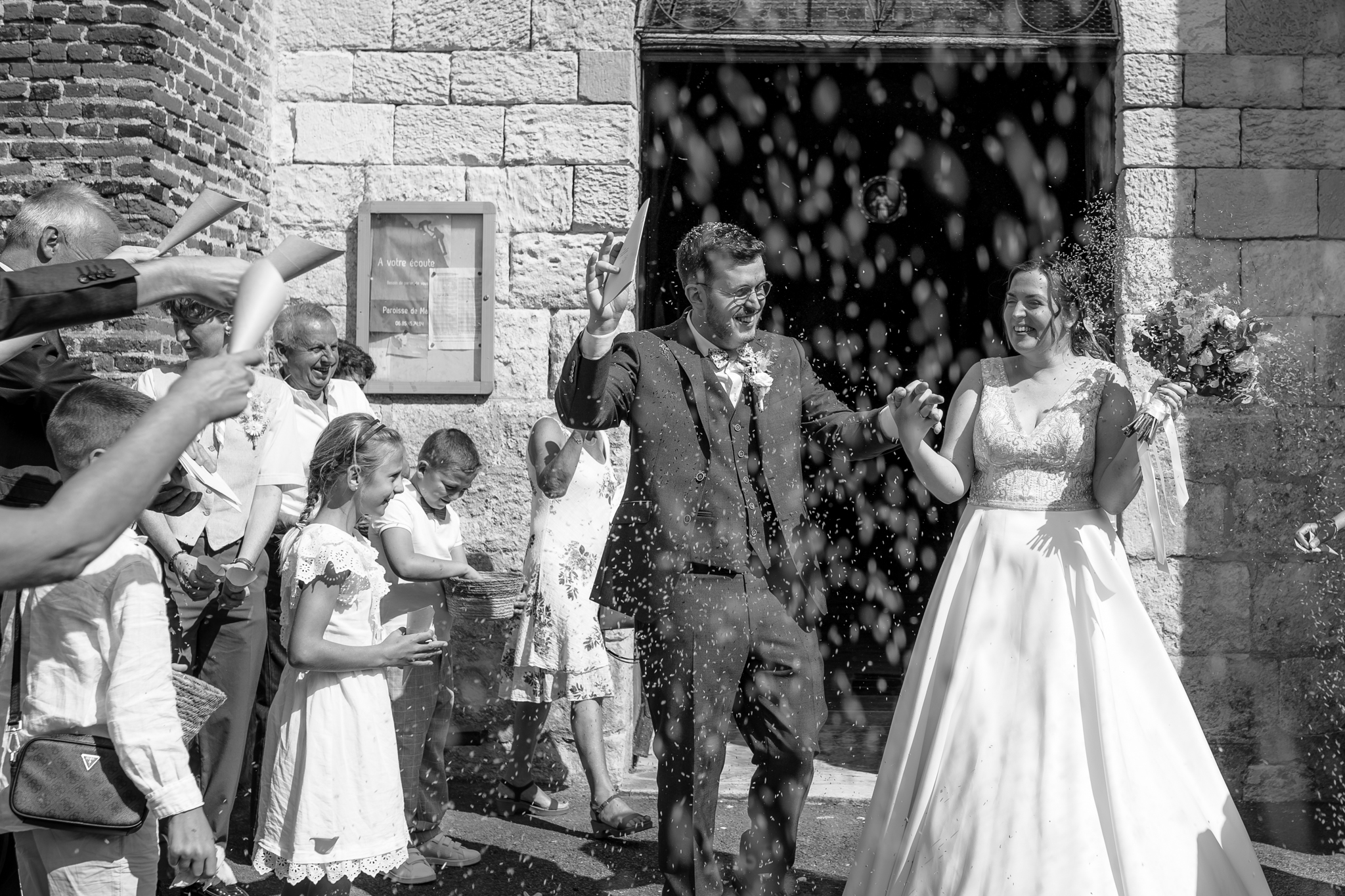 Les mariés qui s’embrassent à la sortie de la cérémonie, entourés de leurs proches qui lancent des pétales.